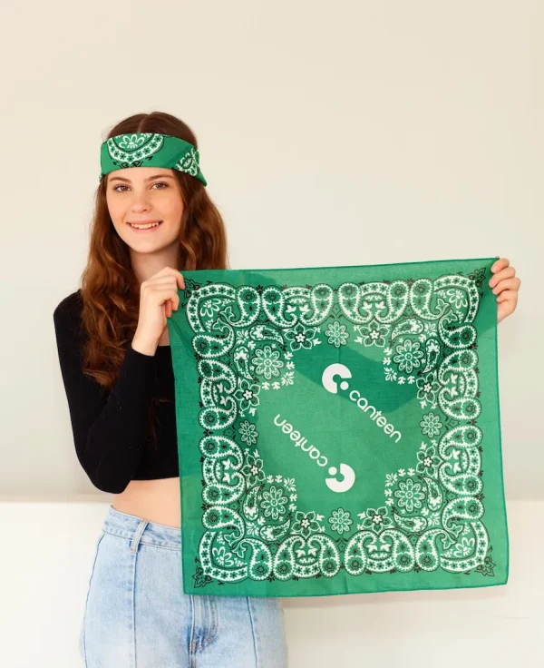 young person wearing a green bandana on her head and holding up the green bandana with a Mexican design in her hands