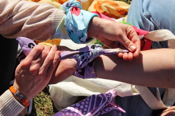 A person tying a Horses Tinkt bandanna on another person's wrist